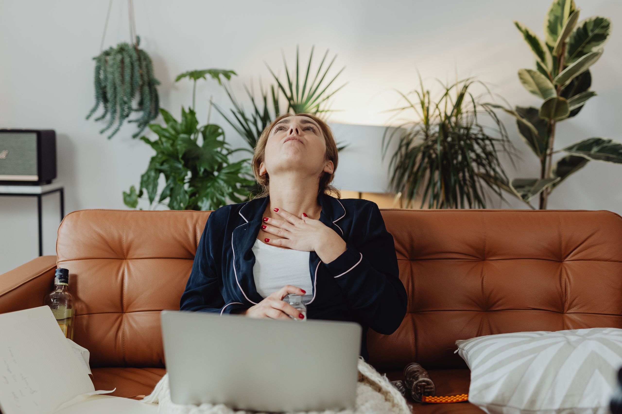 Woman in pajamas sitting on a brown leather couch, relaxing with plants and decor around.