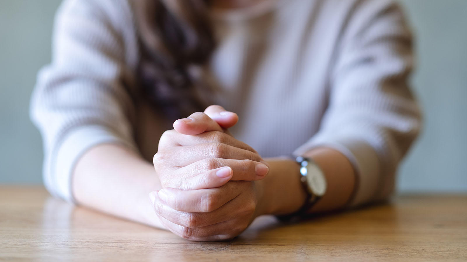 Tightly clasped hands at a table, the physical tension characteristic of depression with anxious distress