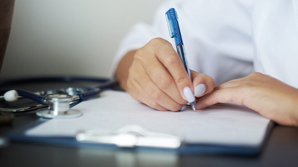 Clinician writing a referral note to a psychiatrist on a clipboard