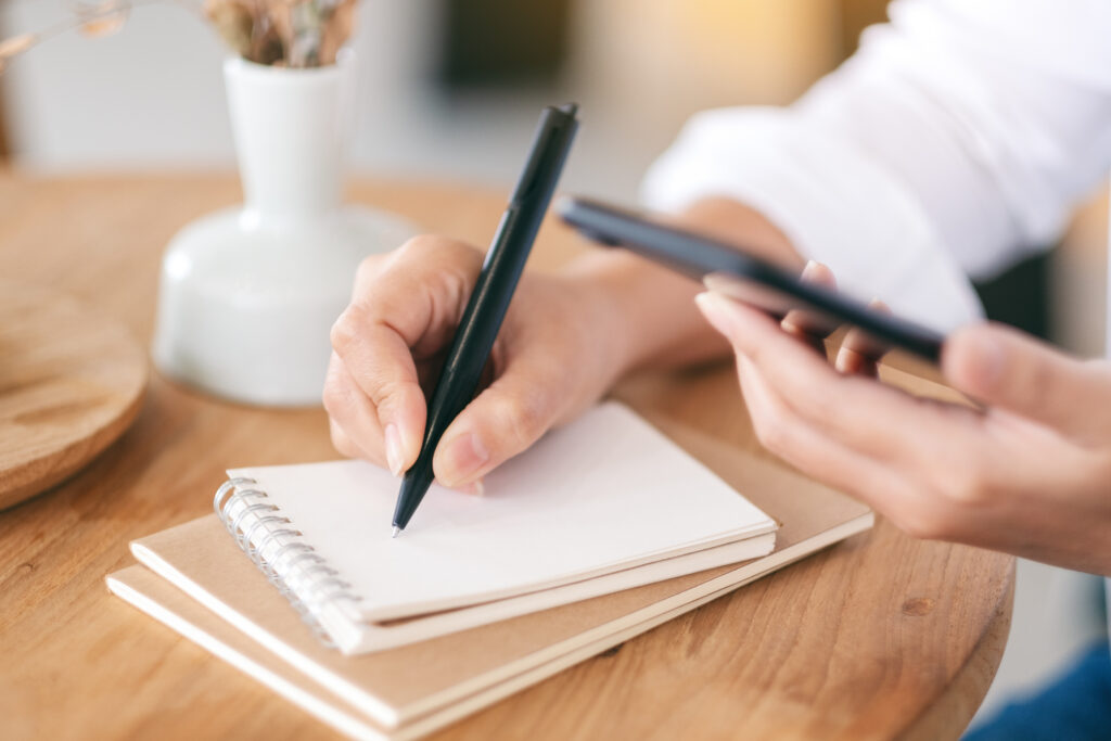 Person checking a phone and writing a short list of psychiatry practices in a notebook